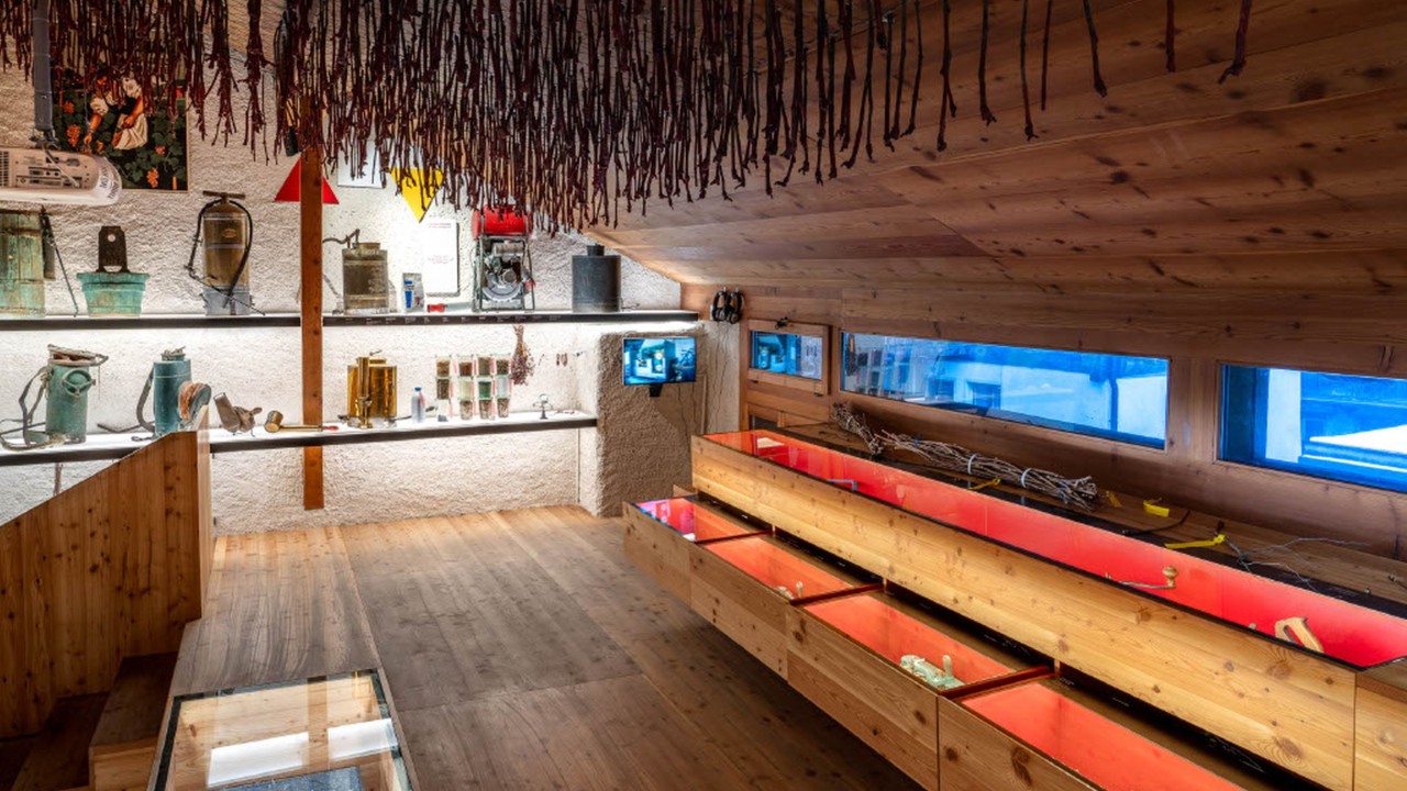 Unter dem mit Kiefernholz getäferten Dachstock des Weinmuseums Salgesch ist an der Rückwand traditionelles Winzerwerkzeug und Zubehör ausgestellt. Rechts daneben werden in Glasvitrinen viele weitere Exponate zur Schau gestellt.